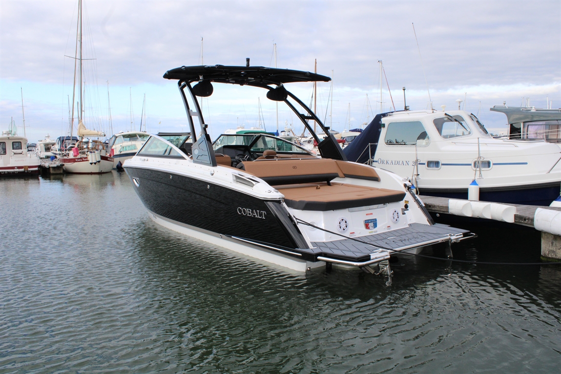 Cobalt boat docked at a marina, surrounded by various boats, with cloudy skies and calm water reflecting the scene.